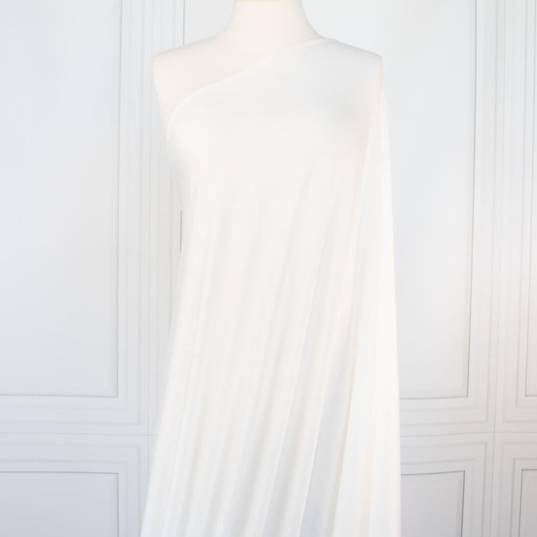 Los Angeles Designer modal jersey knit deadstock fabric by the yard is sustainability at its best. A soft and smooth off-white knit fabric with a cool hand and fluid drape, perfect for a T-shirt, camisole, or loungewear. Long image of fabric on dressform.