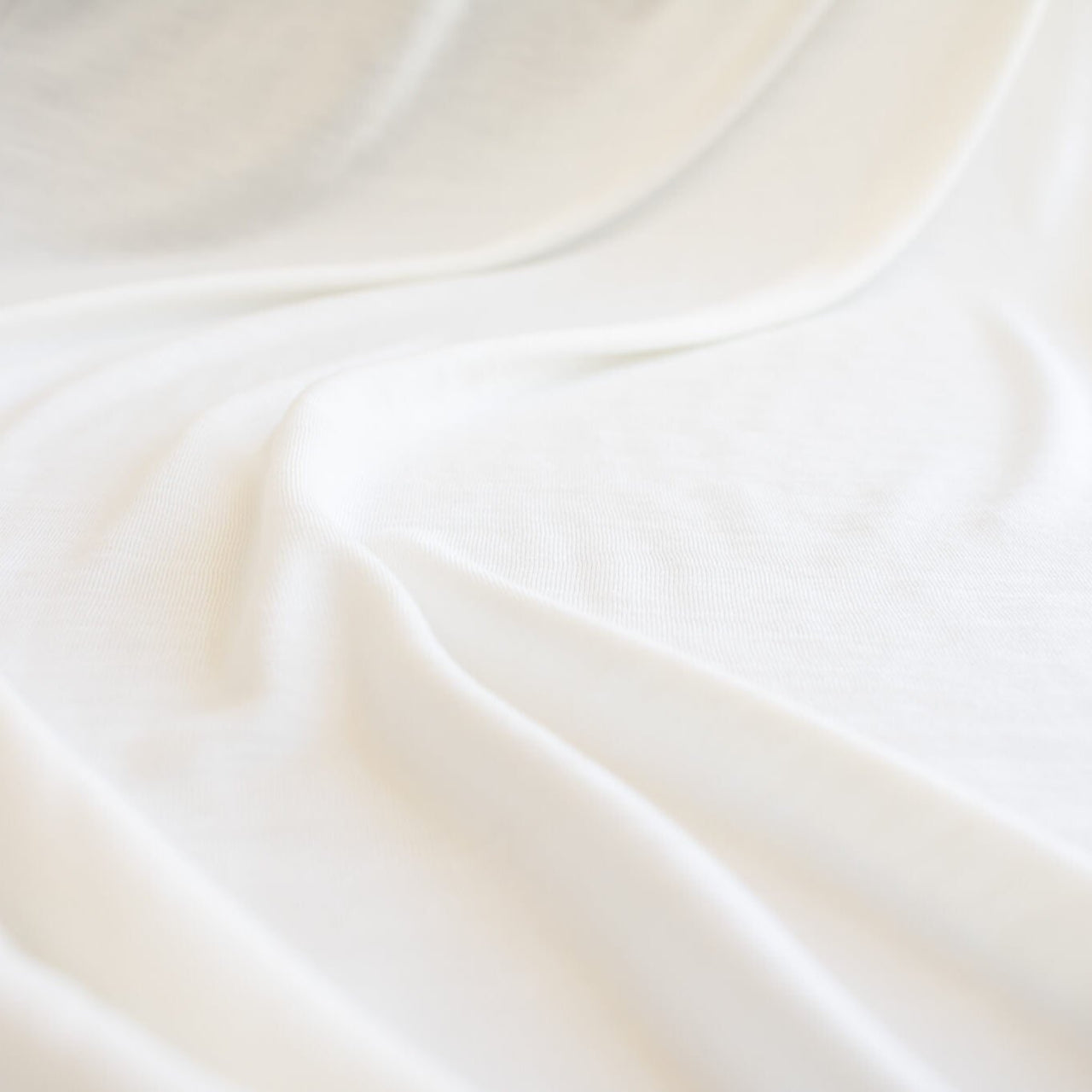 Los Angeles Designer modal jersey knit deadstock fabric by the yard is sustainability at its best. A soft and smooth off-white knit fabric with a cool hand and fluid drape, perfect for a T-shirt, camisole, or loungewear. Close up image.