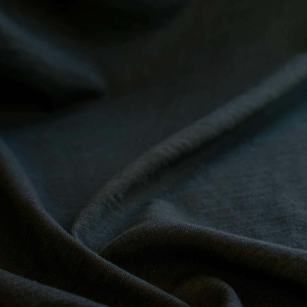 NYC High-End Designer Black Cotton Jersey Knit fabric by the yard. This deadstock fabric is the perfect sustainable choice for creating soft, flowy pieces that are both stylish and playful. It has a soft hand and translucent quality, and the extra wide width allows for versatile designs. Close up image.