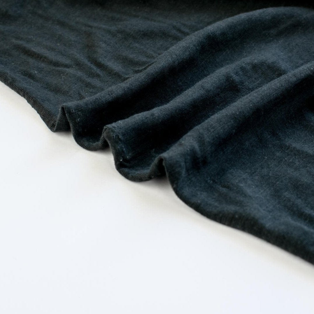 NYC High-End Designer Black Cotton Jersey Knit fabric by the yard. This deadstock fabric is the perfect sustainable choice for creating soft, flowy pieces that are both stylish and playful. It has a soft hand and translucent quality, and the extra wide width allows for versatile designs. Image of selvedge.
