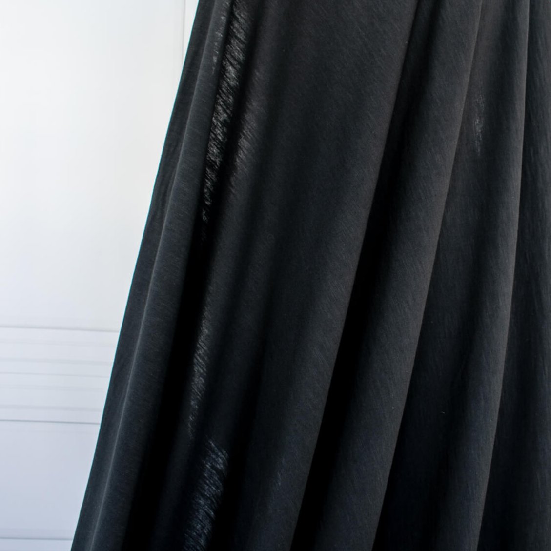 NYC High-End Designer Black Cotton Jersey Knit fabric by the yard. This deadstock fabric is the perfect sustainable choice for creating soft, flowy pieces that are both stylish and playful. It has a soft hand and translucent quality, and the extra wide width allows for versatile designs. Image of fabric drape.
