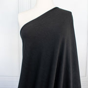 NYC High-End Designer Black Cotton Jersey Knit fabric by the yard. This deadstock fabric is the perfect sustainable choice for creating soft, flowy pieces that are both stylish and playful. It has a soft hand and translucent quality, and the extra wide width allows for versatile designs. Image of fabric on dressform.