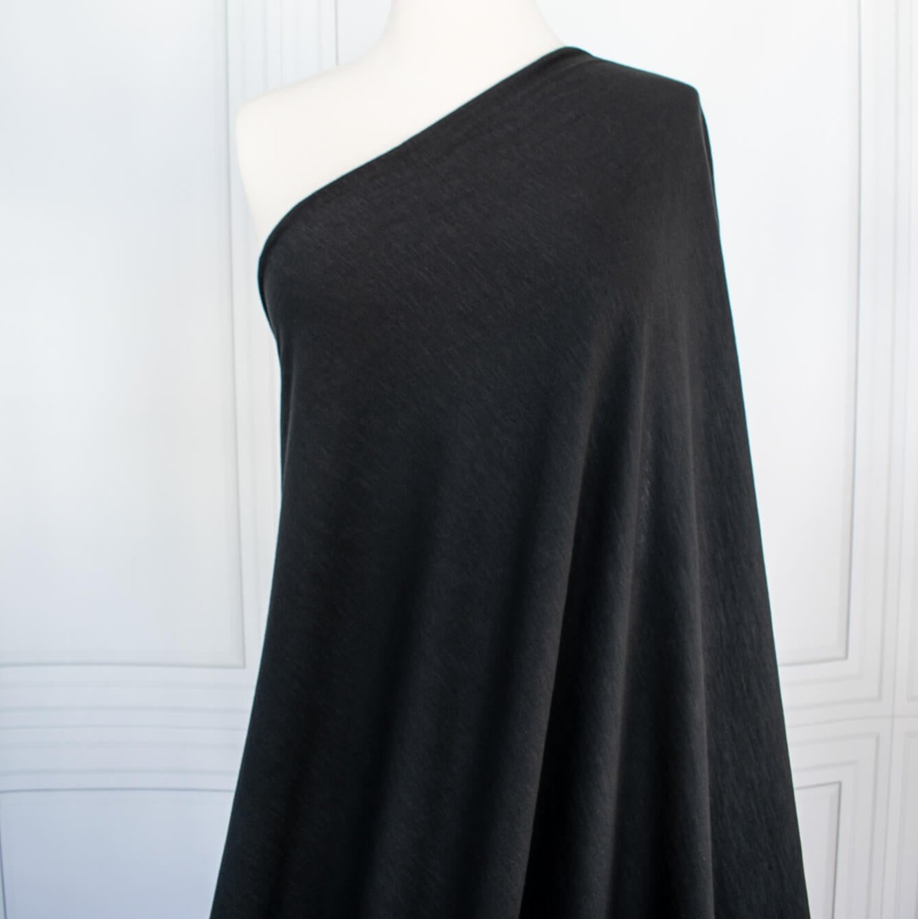 NYC High-End Designer Black Cotton Jersey Knit fabric by the yard. This deadstock fabric is the perfect sustainable choice for creating soft, flowy pieces that are both stylish and playful. It has a soft hand and translucent quality, and the extra wide width allows for versatile designs. Image of fabric draped on dress from.