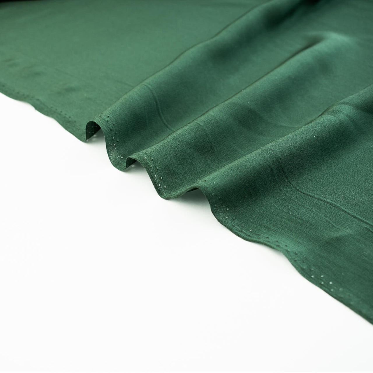 00% Silk Crepe de Chine fabric by the yard in Fern Green. Soft and fluid, this semi-textured fabric offers a beautiful drape and the luxury of silk. Image of selvedge.