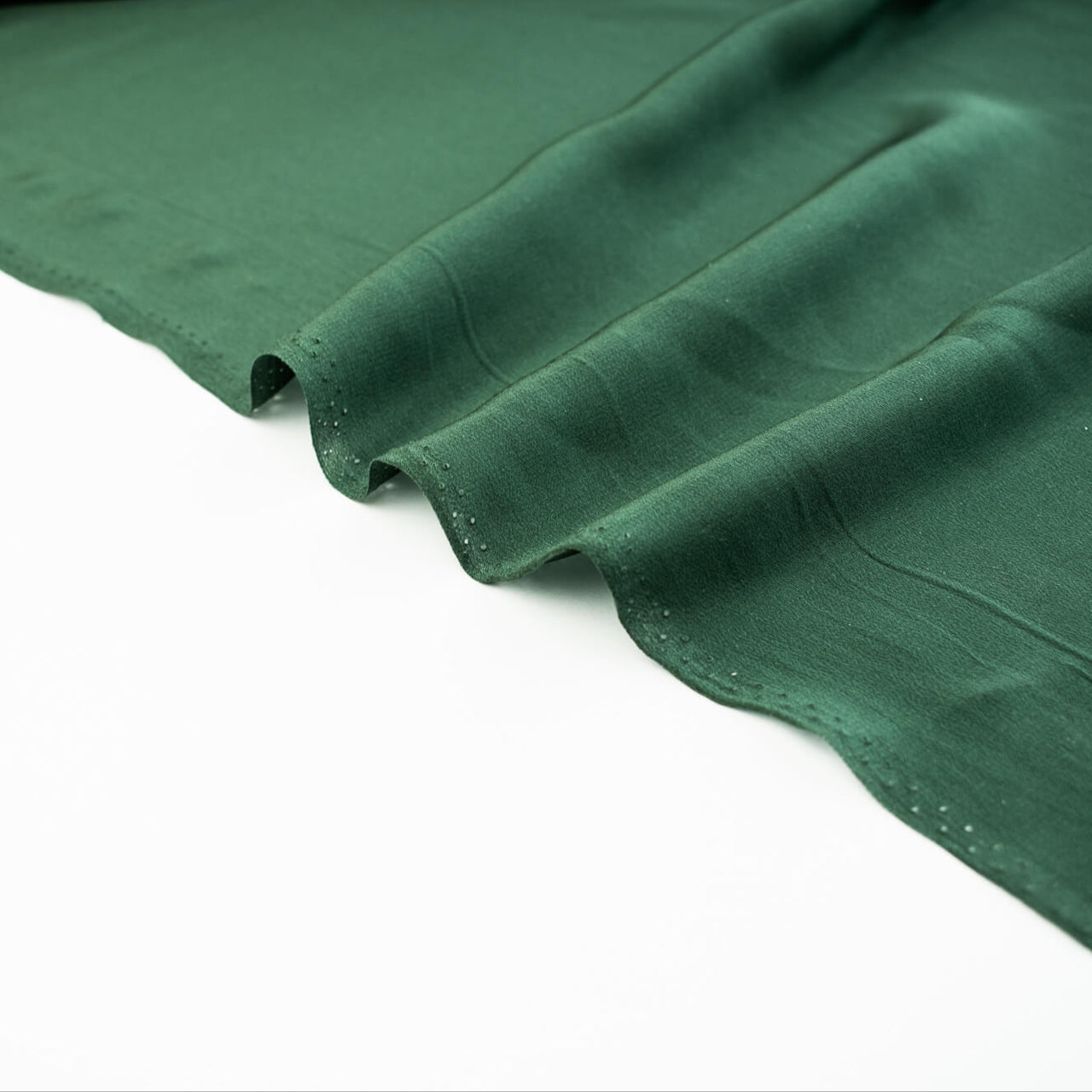 00% Silk Crepe de Chine fabric by the yard in Fern Green. Soft and fluid, this semi-textured fabric offers a beautiful drape and the luxury of silk. Image of selvedge.
