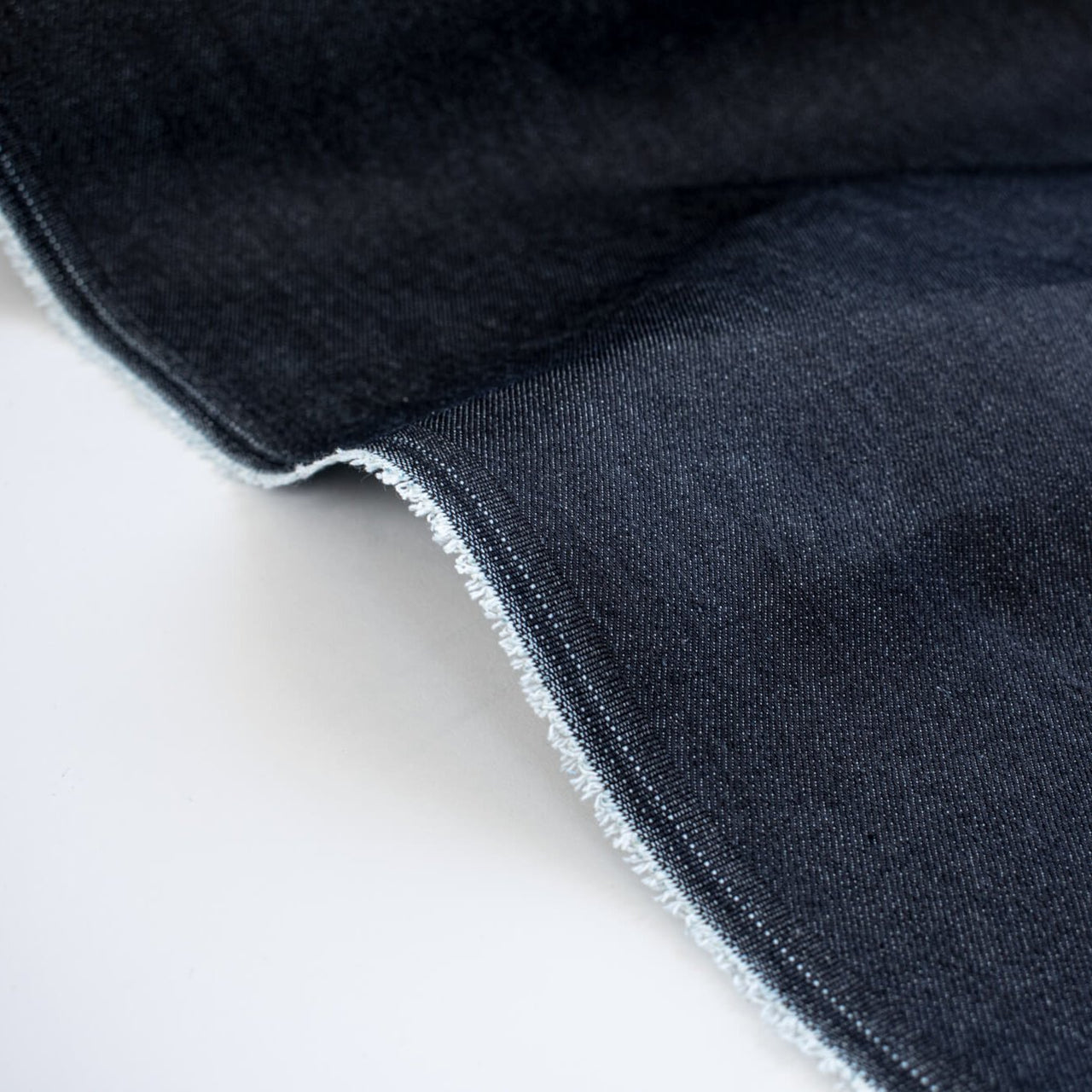 Get the perfect blend of comfort and style with our Midnight Navy Cotton Stretch Denim Twill fabric by the yard.  A denim you can dress up with its deep rich dark blue color and crisp, semi-textured hand. Close up image of selvedge.