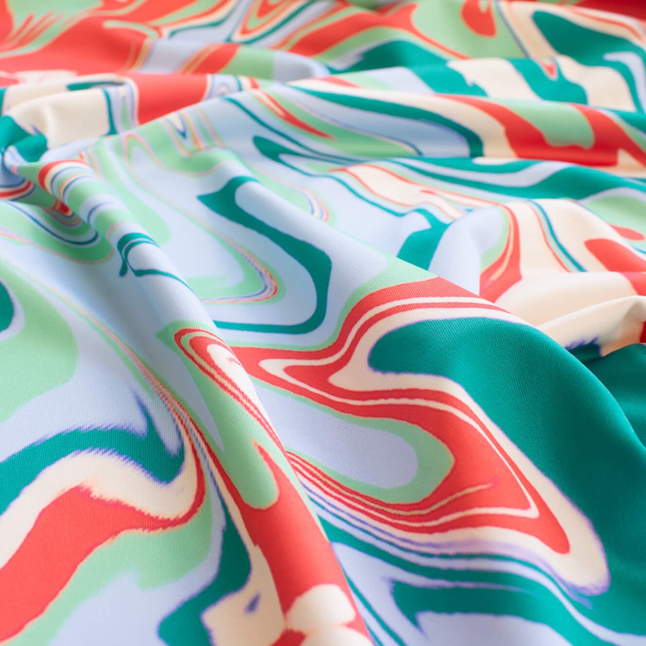 NYC Designer Abstract Jesery Knit designer deadstock fabric by the yard. A mid-weight opaque jersey knit with a soft, smooth hand and slight sheen. Shades of light blue, sea glass green, turquoise green, and coral evoke a playful and fun mood with colors hinting at 'Miami Vibes'. Close up image.