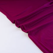 Famous Designer Poly/Spandex ITY Knit in 'Berry Rich'! This designer deadstock fabric by the yard boasts a rich berry color that is sure will elevate any project. Its smooth hand and elegant drape is a must have for comfort and style. Image of fabric selvedge.