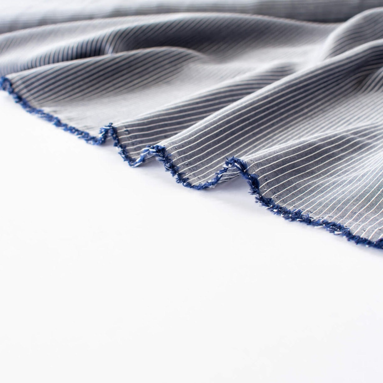  NYC Designer Deadstock Cotton Voile fabric by the yard. Amazingly soft and silky, this Navy/White horizontal stripe voile is lightweight with a thin hand, a must for warmer temperatures. Image of fabric selvedge.