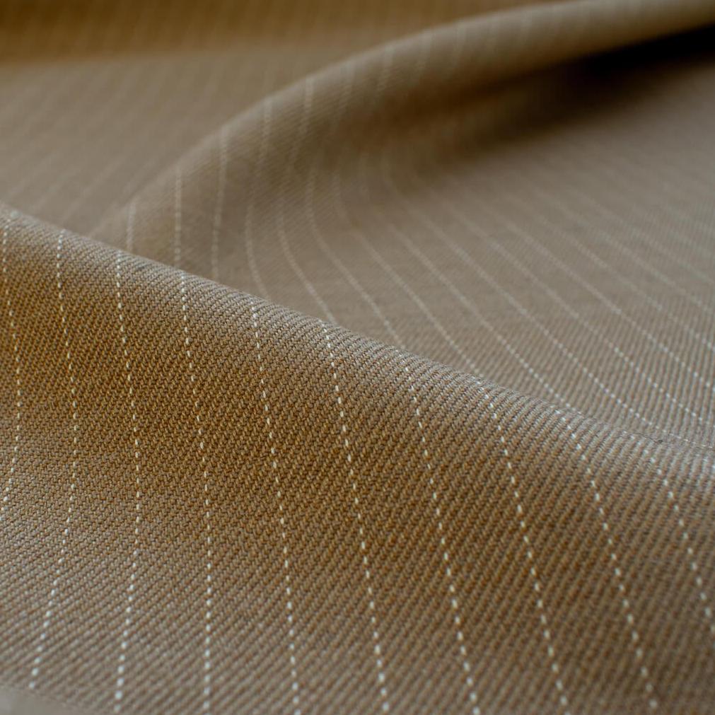 This elegant NYC Designer Pinstripe Twill designer deadstock fabric by the yard is the perfect choice for those who appreciate understated elegance. The gorgeous combination of tan highlighted by a white pinstripe features a soft, textured hand and falls moderately away from the body. A perfect choice if you will be sewing up a trouser, or suiting. Close up image.