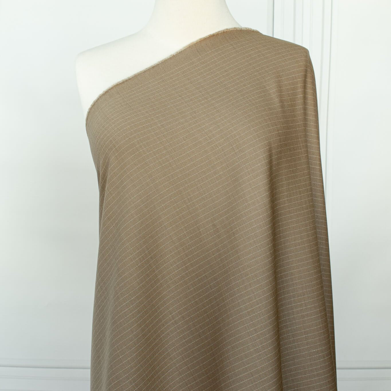 This elegant NYC Designer Pinstripe Twill designer deadstock fabric by the yard is the perfect choice for those who appreciate understated elegance. The gorgeous combination of tan highlighted by a white pinstripe features a soft, textured hand and falls moderately away from the body. A perfect choice if you will be sewing up a trouser, or suiting. Longer image of fabric draped on dressform.