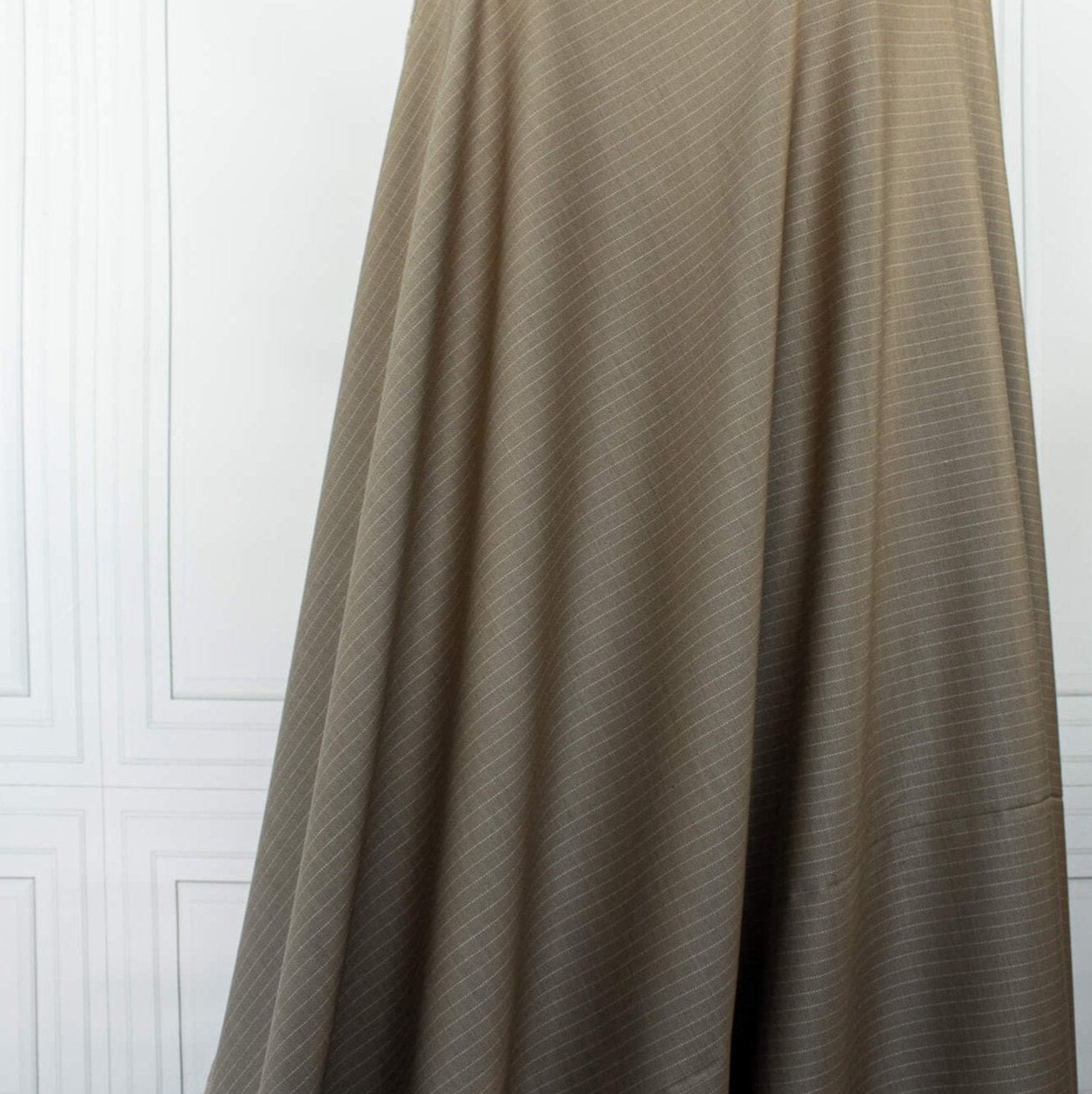 This elegant NYC Designer Pinstripe Twill designer deadstock fabric by the yard is the perfect choice for those who appreciate understated elegance. The gorgeous combination of tan highlighted by a white pinstripe features a soft, textured hand and falls moderately away from the body. A perfect choice if you will be sewing up a trouser, or suiting.  Image of fabric drape.