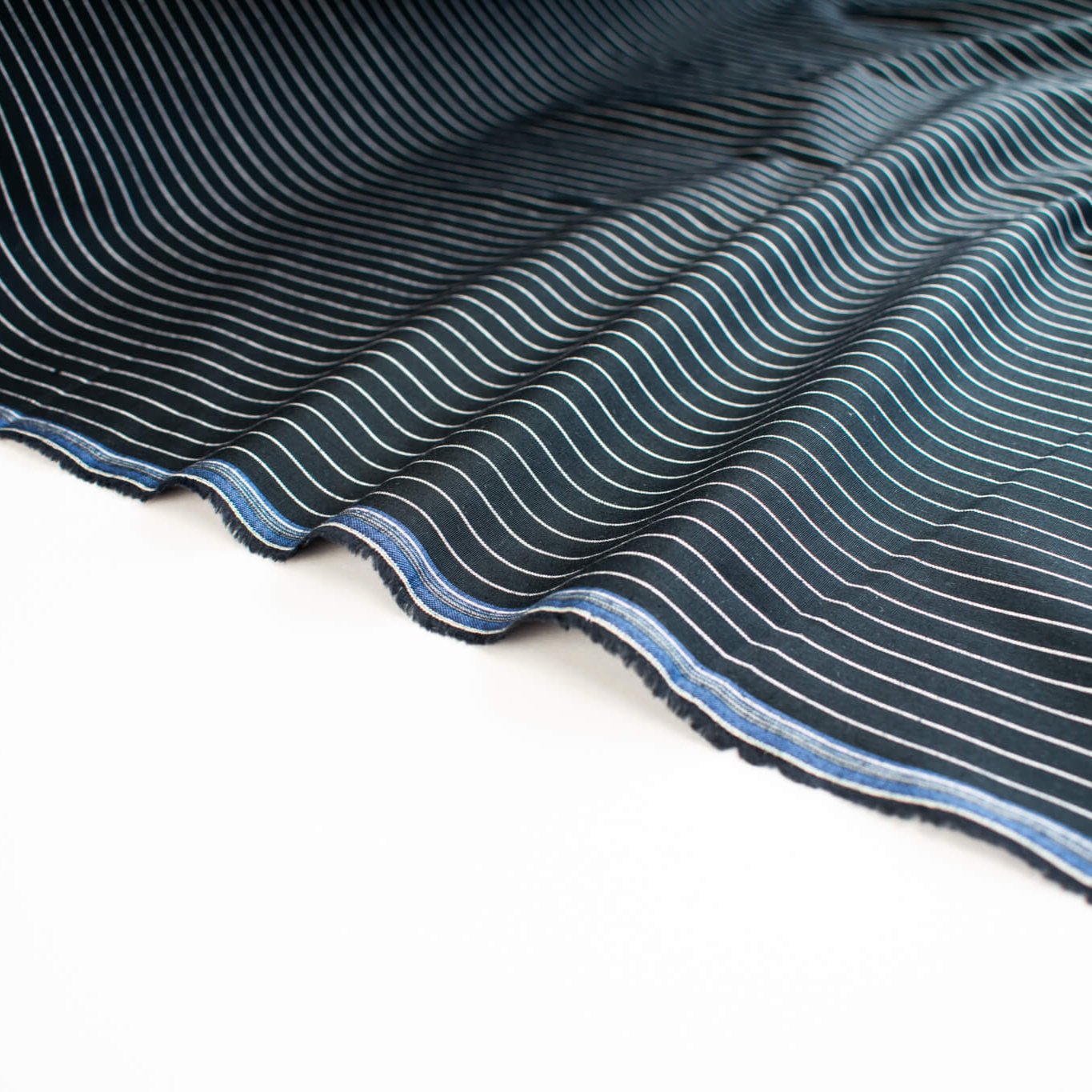 NYC Designer Dark Navy/White Striped Cotton/Spandex Shirting fabric by the yard in a midnight blue is a perfect staple when building your wardrobe pieces. This designer deadstock fabric boasts a soft and smooth hand, is tightly woven and enhanced with a touch of stretch. Image of Selvedge.