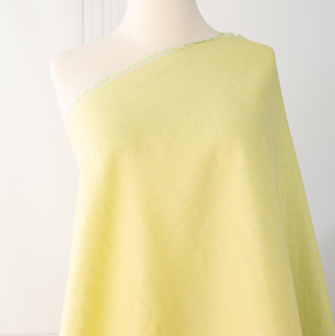 Made of 100% linen, this shirt-weight fabric features a gentle blend of spring green, white, and soft yellow tones, perfect for a stylish shirt, dress or skirt. Enjoy the lightweight, soft semi-crisp hand of this cross-dyed, woven fabric. Image of fabric draped on dressform.