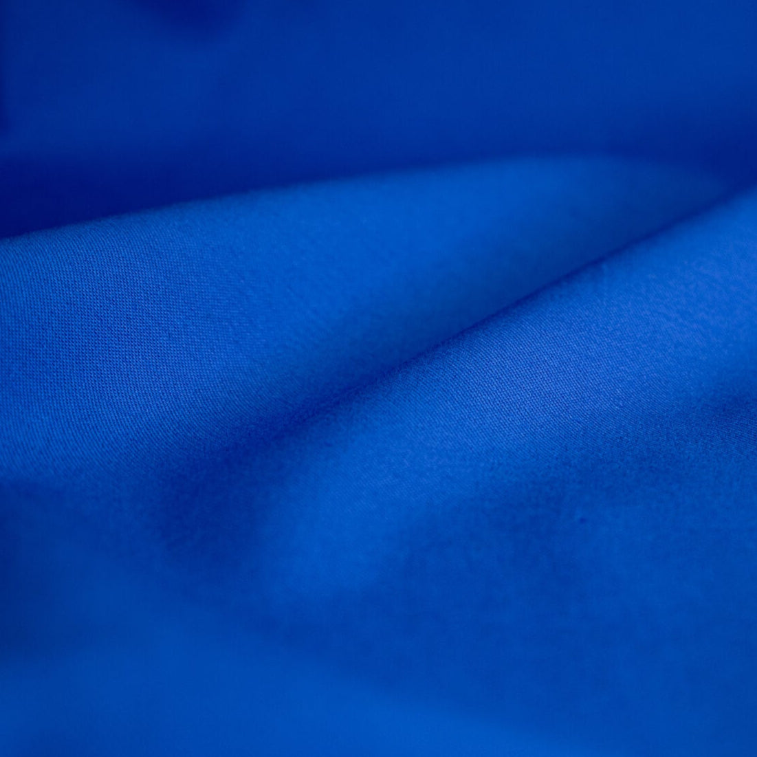 Royal Blue Cotton Lycra Stretch Sateen woven fabric by the yard. The satin weave in this lovely bottom-weight fabric creates a lustrous, soft, and crisp hand with a slight sheen. Create a fun jacket, pant or dress in this rich royal blue you are sure to love. Close up image.