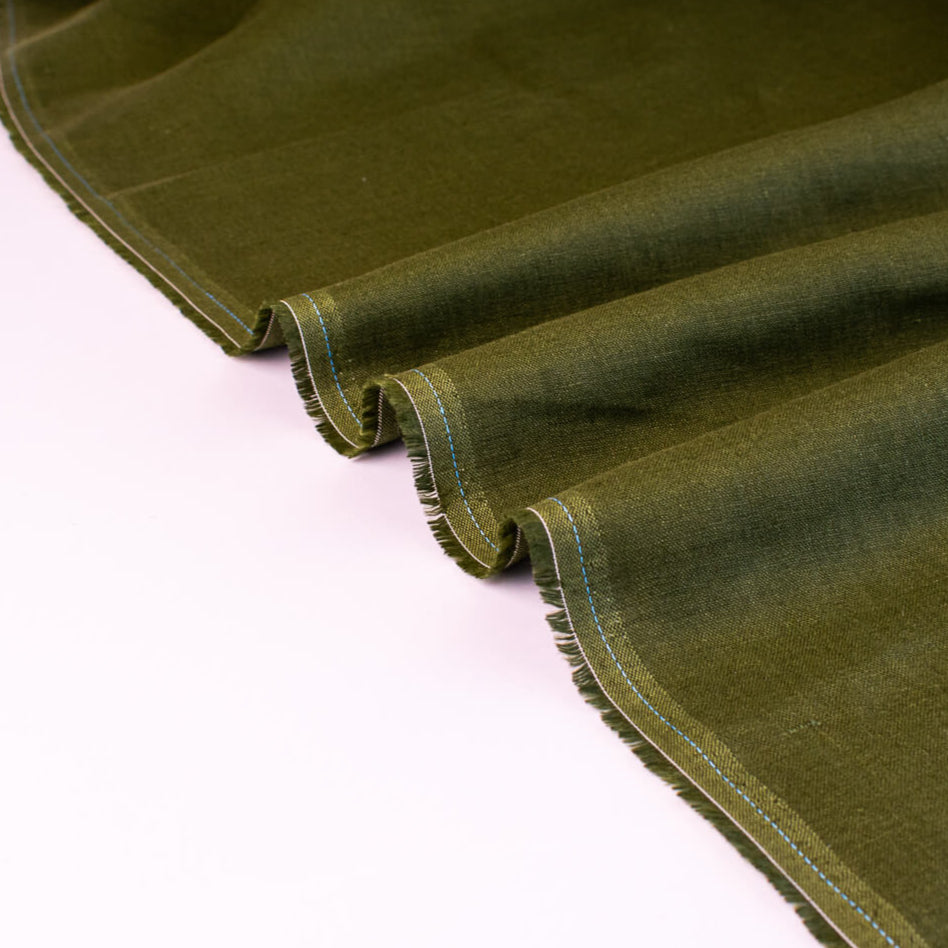This stunning deep green 100% Linen shirtweight fabric by the yard is sure to become a wardrobe staple. A soft crisp hand and a drape that falls moderately away from the body is perfect for your next linen project. Image of selvedge.