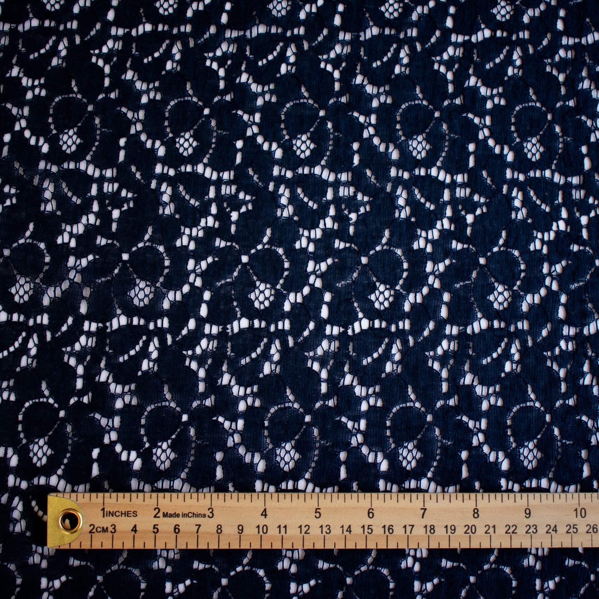 Navy blue fabric with lace pattern and a ruler at the bottom for scale.