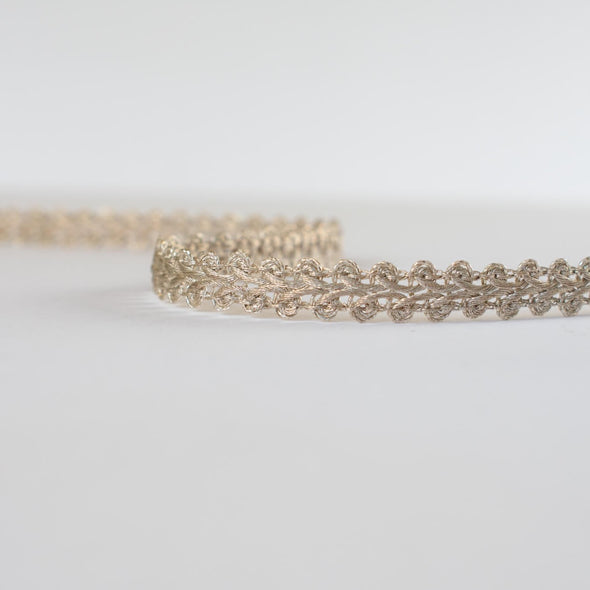 This stunning vintage gimp trim is the perfect addition to any couture garment. Our narrow trim is crafted from a mix of silver and champagne gold metallic threads, making it a designer's dream. A timeless piece, this trim is sure to elevate any project with its timeless charm.