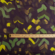 A close-up image of  Italian viscose sateen  fabric by the yard in deep eggplant adorned with modern abstract brushstrokes in olive, fern green, and golden yellow, with a wooden ruler laid horizontally for scale.