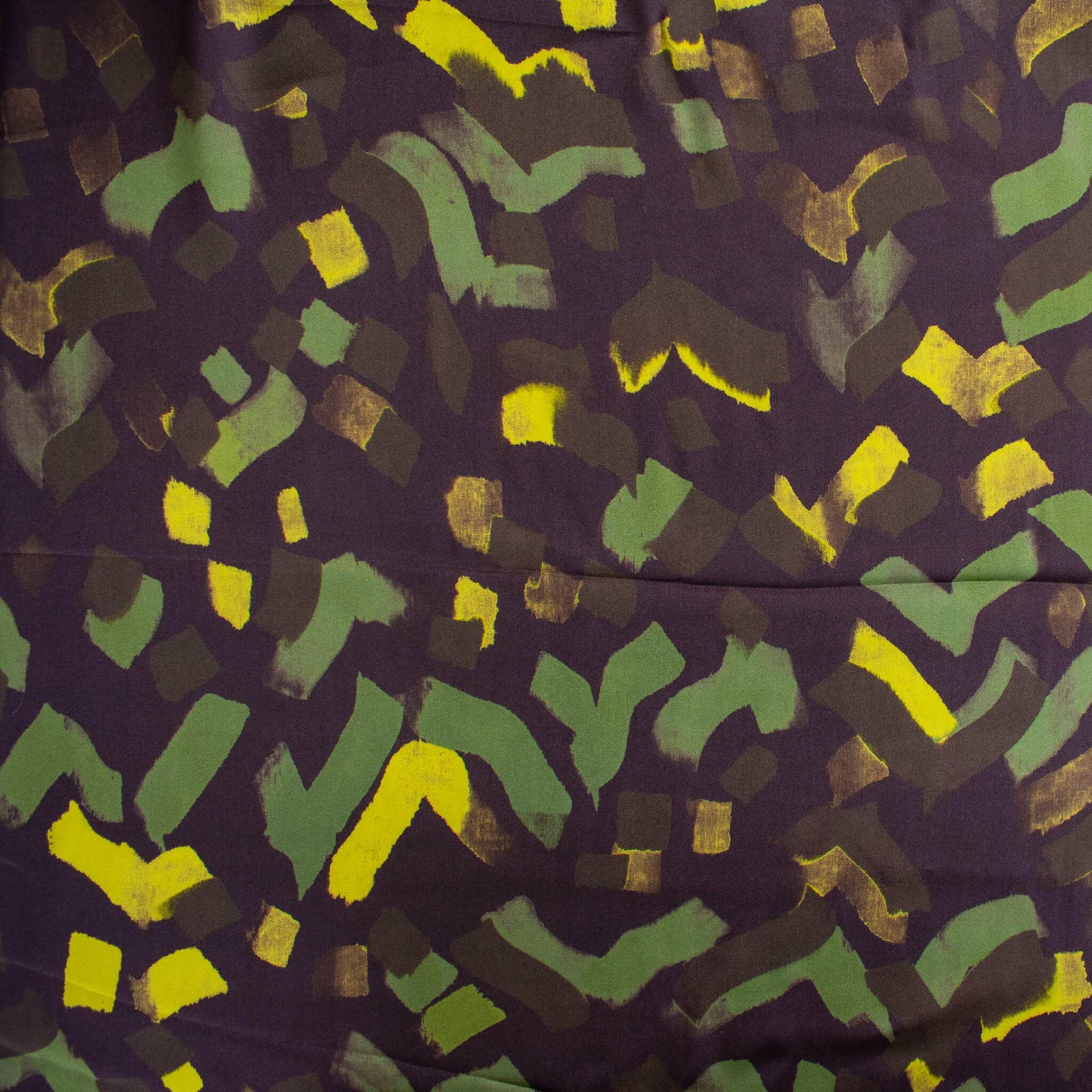 A close-up of a patterned fabric featuring abstract, hand-painted style brushstrokes in green, bright yellow, and dark brown on a deep purple background.