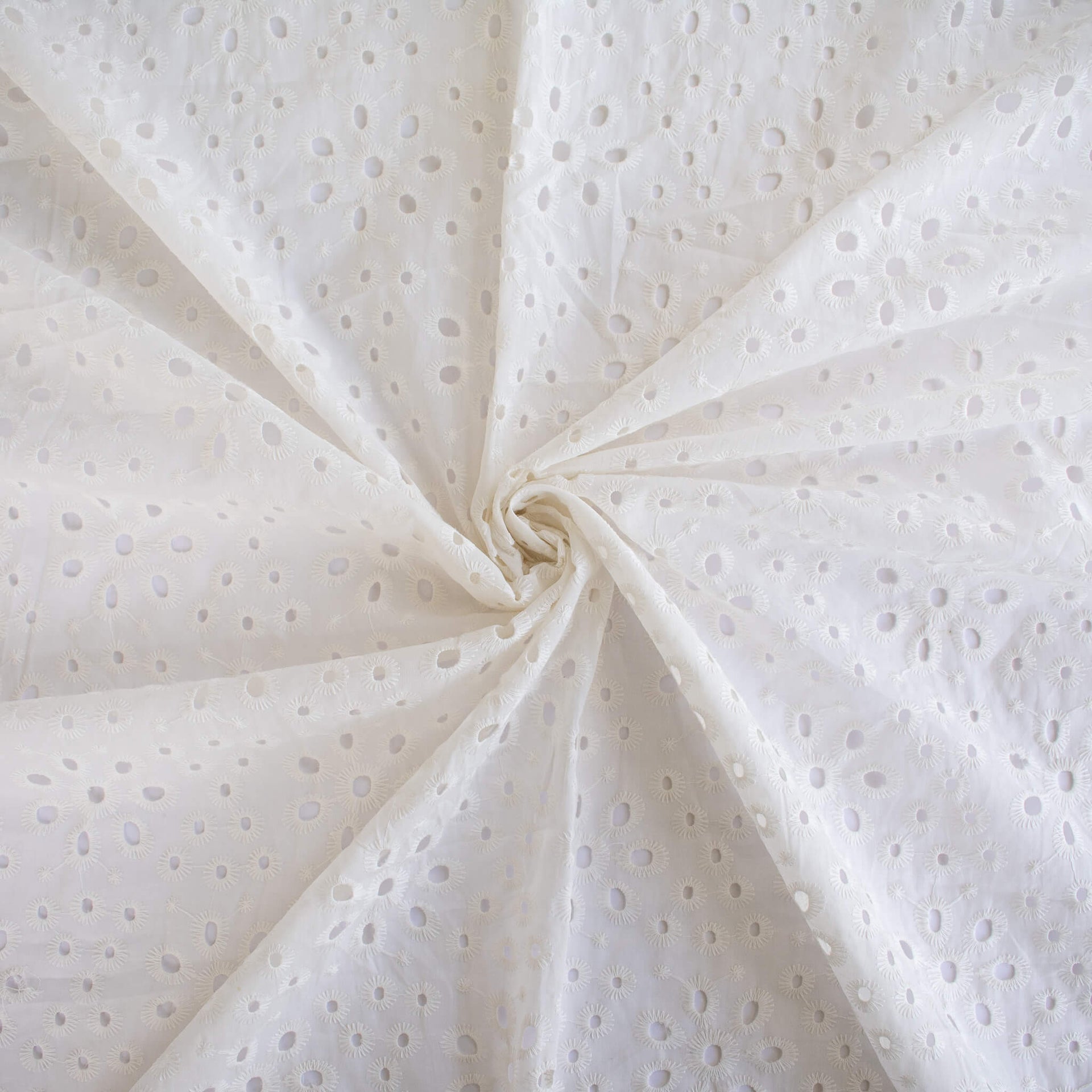 Image of  Italian Cotton San Gallo Lace in soft white, a delicate broderie anglaise fabric swirled to demonstrate fullness.