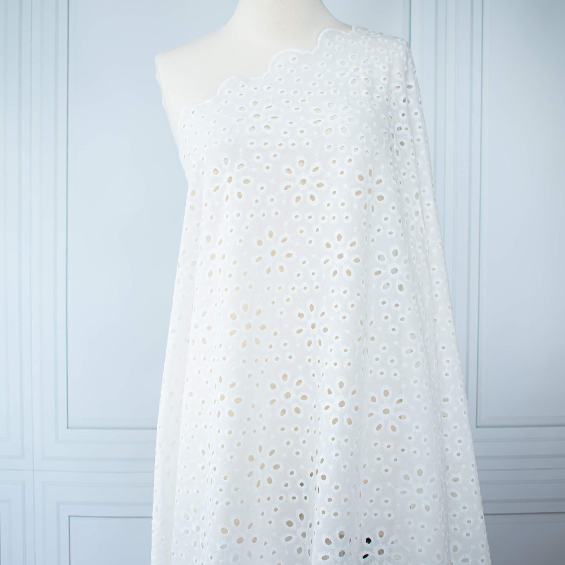 Image of  Italian Cotton San Gallo Lace in soft white, a delicate broderie anglaise fabric draped on dress form.
