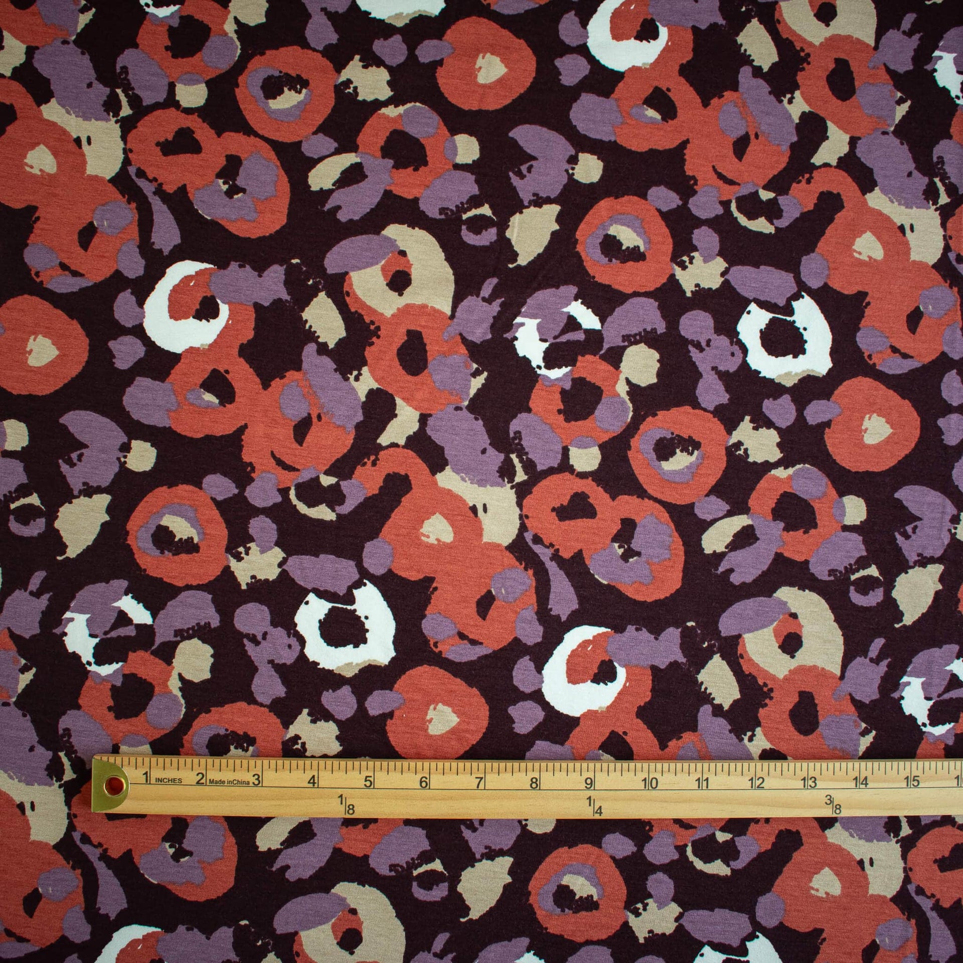 A close-up of  Italian Cotton Jersey Warm Abstract Print fabric with a wooden ruler along the bottom edge for scale.