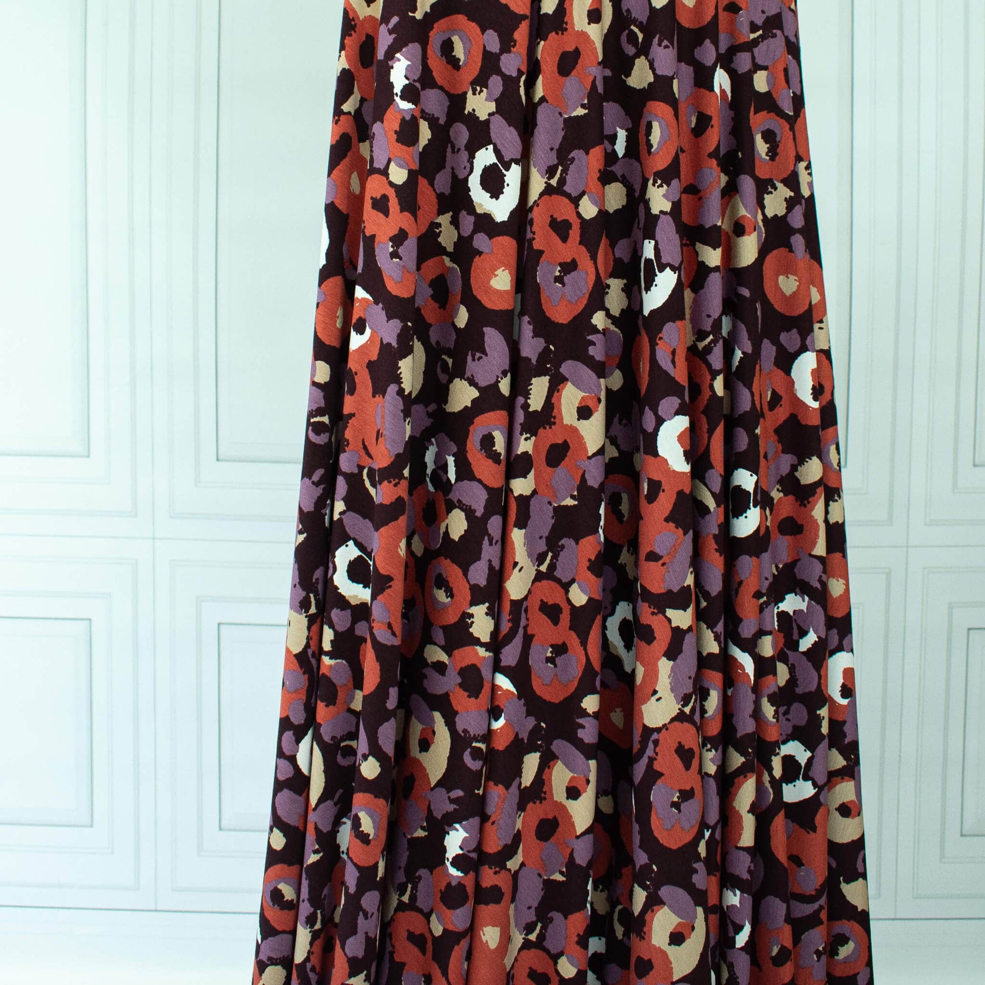 Image of Italian Cotton Jersey Warm Abstract Print fabric draped on dress form 
against a white paneled wall.