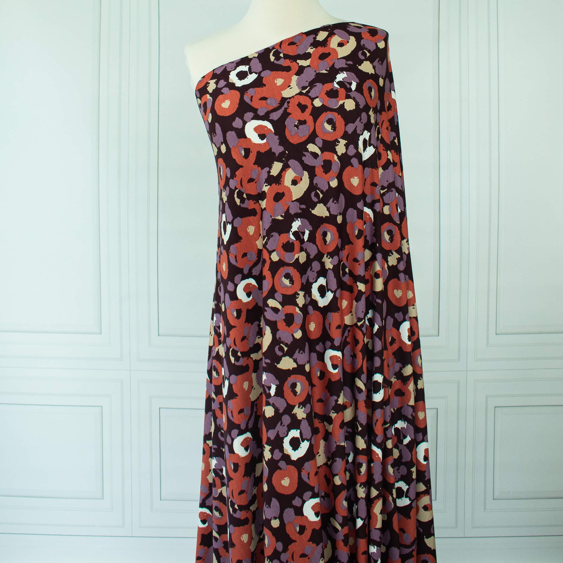 Image of Italian Cotton Jersey Warm Abstract Print fabric draped on dress form 
against a white paneled wall.
