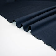A close-up of Couture Italian wool and linen blend navy gabardine fabric draped diagonally across a white surface, showing the material's texture and selvedge