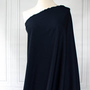 Couture Italian wool and linen blend navy gabardine fabric draped over a white dress form, set against a white paneled wall background.