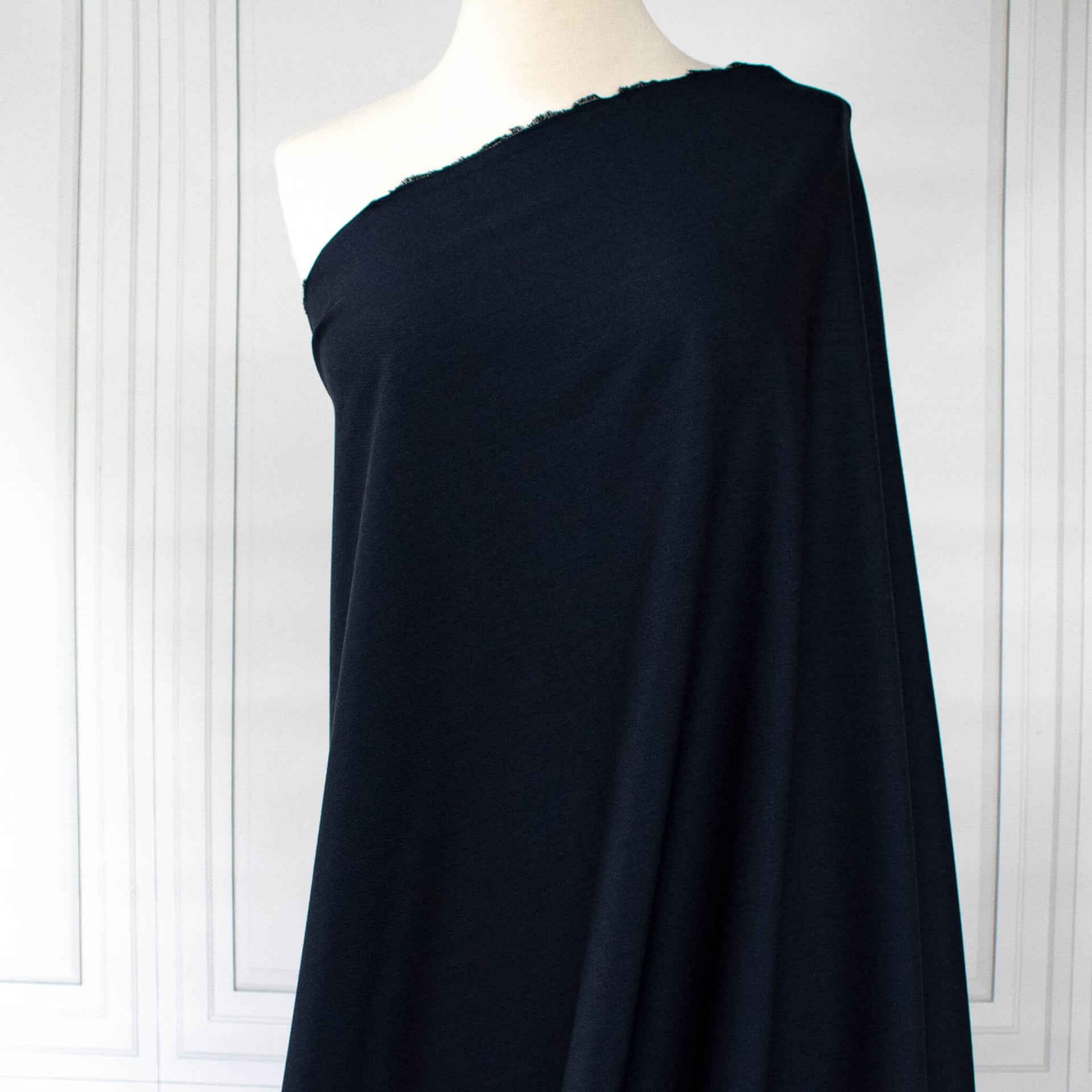Couture Italian wool and linen blend navy gabardine fabric draped over a white dress form, set against a white paneled wall background.