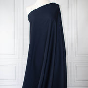 Couture Italian wool and linen blend navy gabardine fabric draped over a white dress form, set against a white paneled wall background.