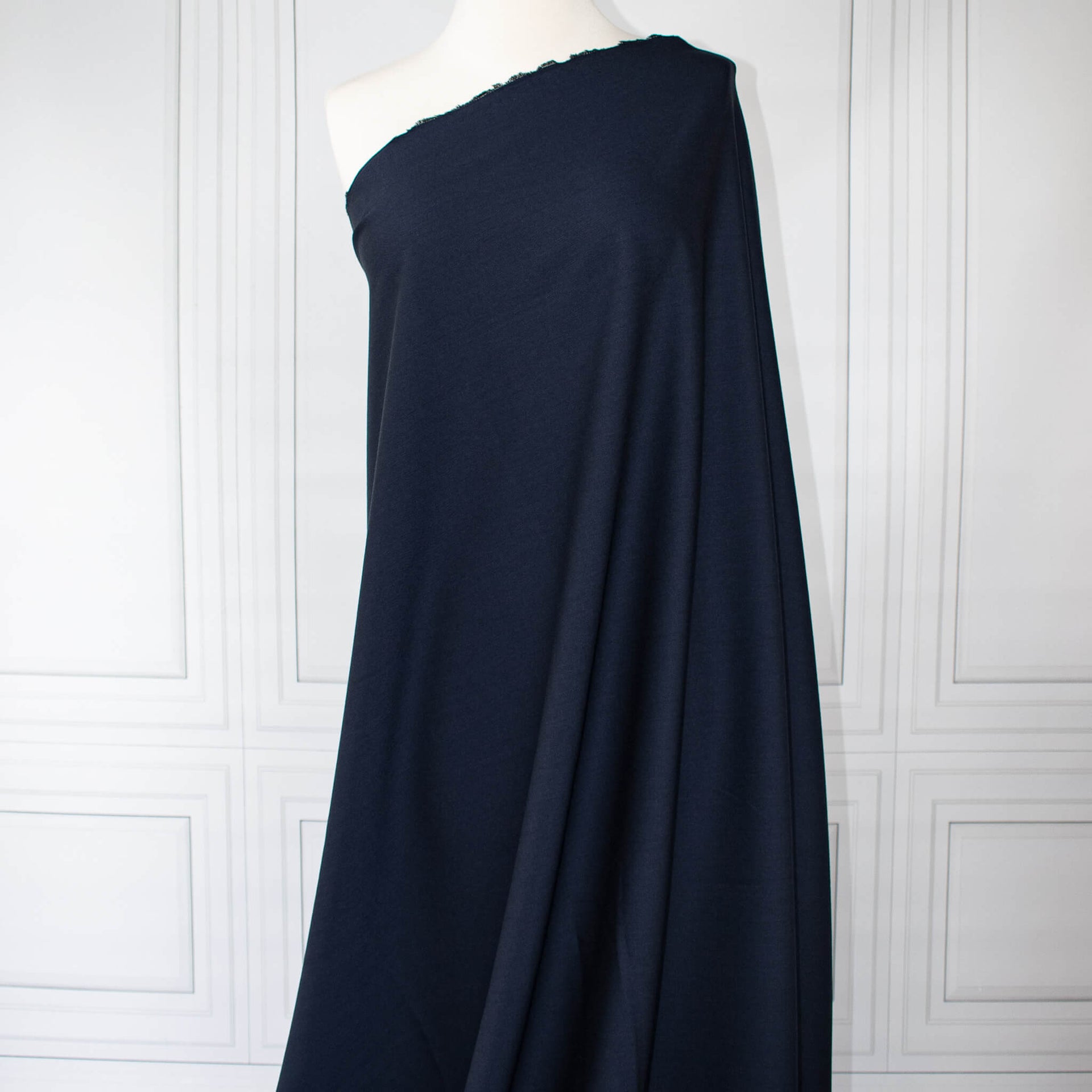 Couture Italian wool and linen blend navy gabardine fabric draped over a white dress form, set against a white paneled wall background.