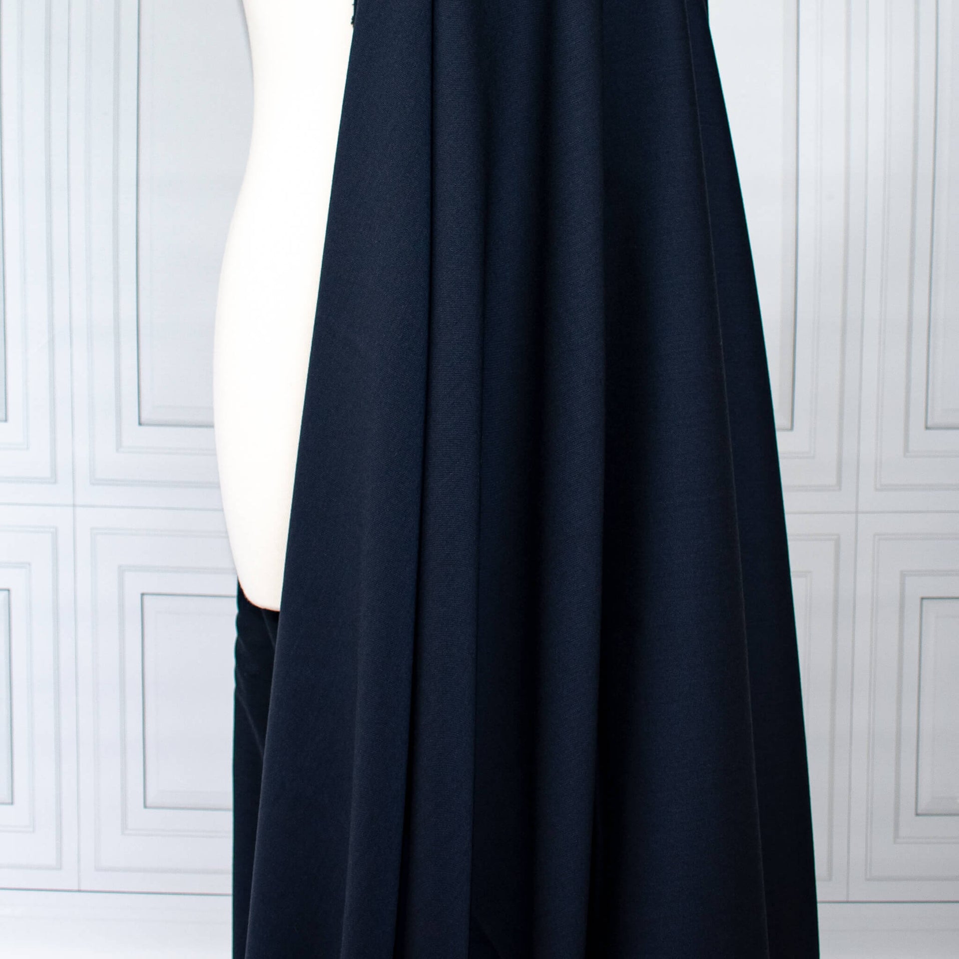 Couture Italian wool and linen blend navy gabardine fabric draped over a white dress form, set against a white paneled wall background.