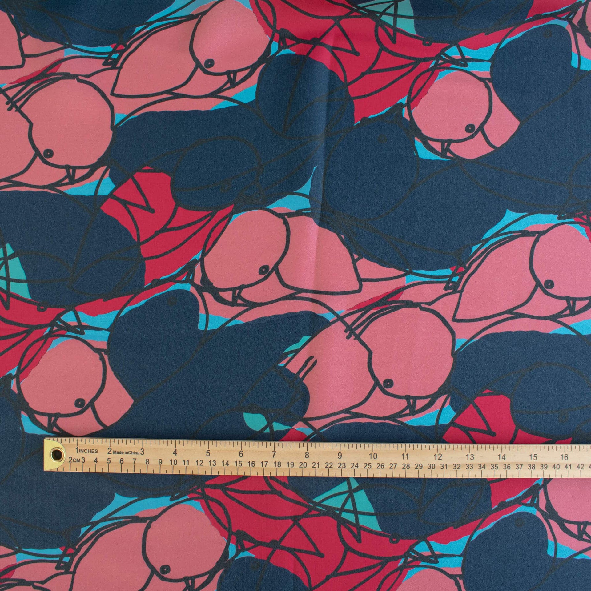 Image of  Italian silk twill fabric by the yard in a modern painterly print with a wooden ruler along the bottom edge for scale. Colors are  coral pink, deep red, and turquoise on a dark navy background. 
