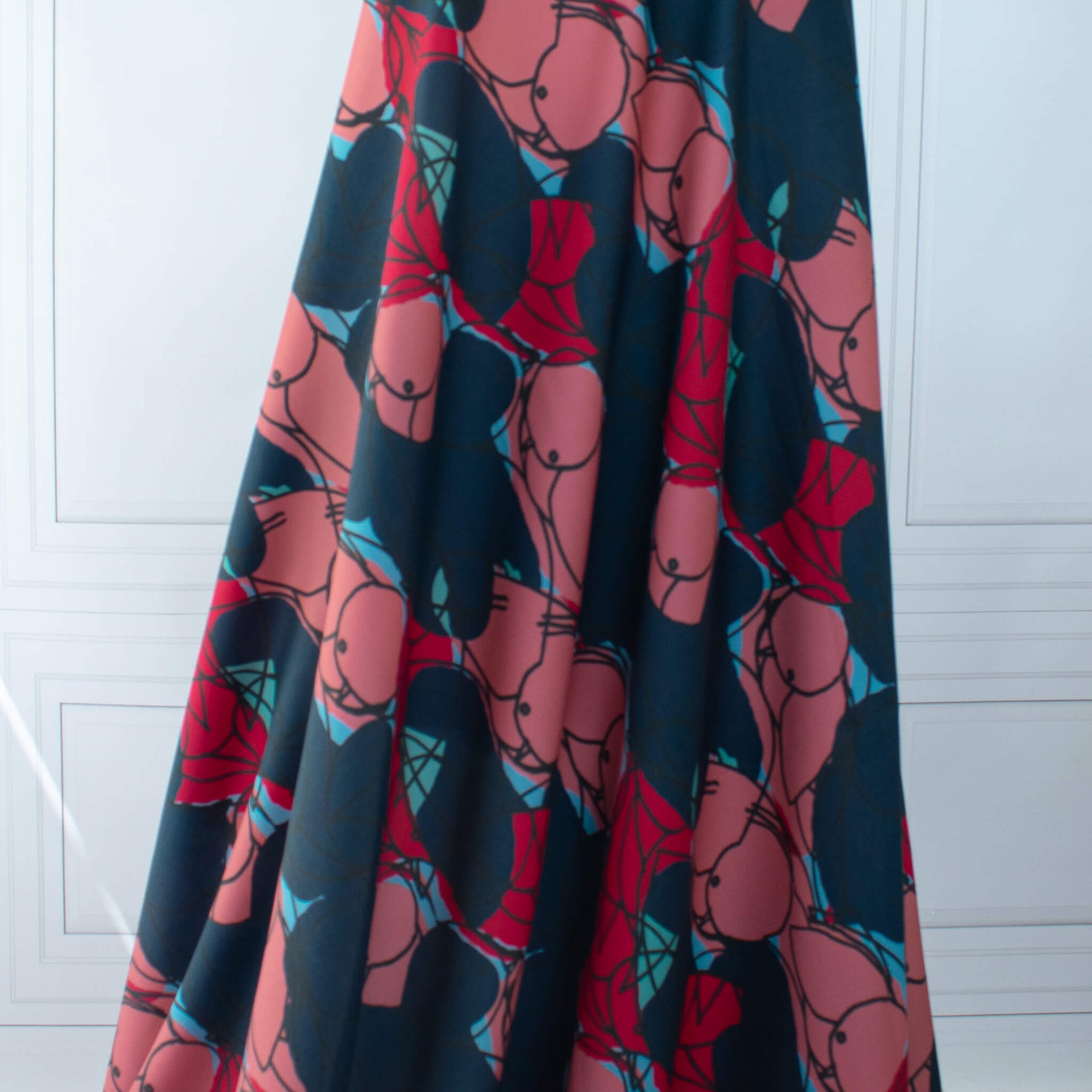 Image of  Italian silk twill fabric by the yard in a modern painterly print draped dress form. Colors are  coral pink, deep red, and turquoise on a dark navy background.