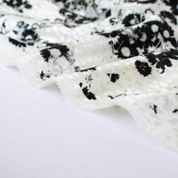 Close up image of couture black and creamy white floral Jacquard. This designer deadstock fabric by the yard features a stunning modern black daisy design set against a white shimmery jacquard.
