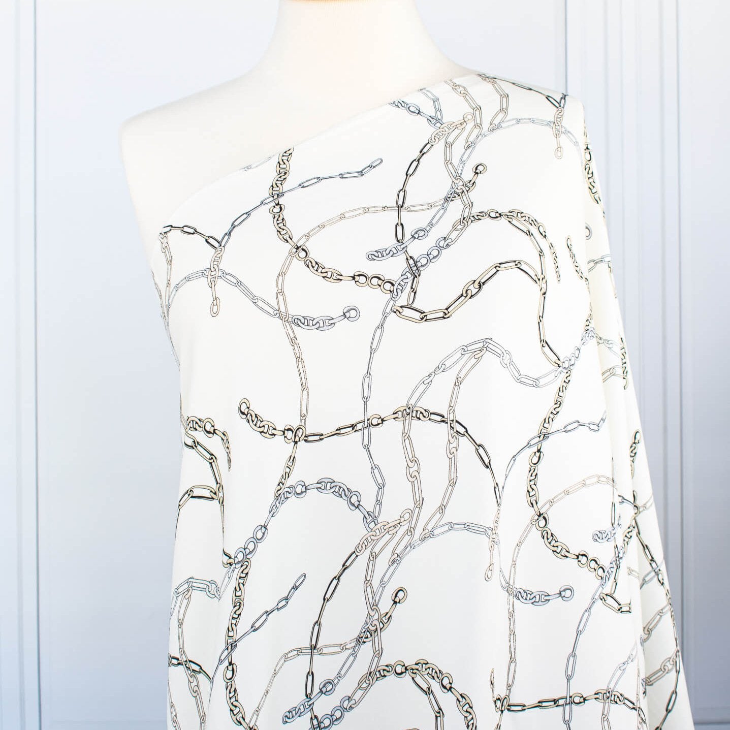 Famous Designer Chain Print Viscose Crepe Faille fabric by the yard. Chain links of tan and grey play upon an ivory background creating a whimsical yet sophisticated look. Slightly translucent with a lightly textured hand, this would make up gorgeous blouse or dress! Image of fabric on dressform.