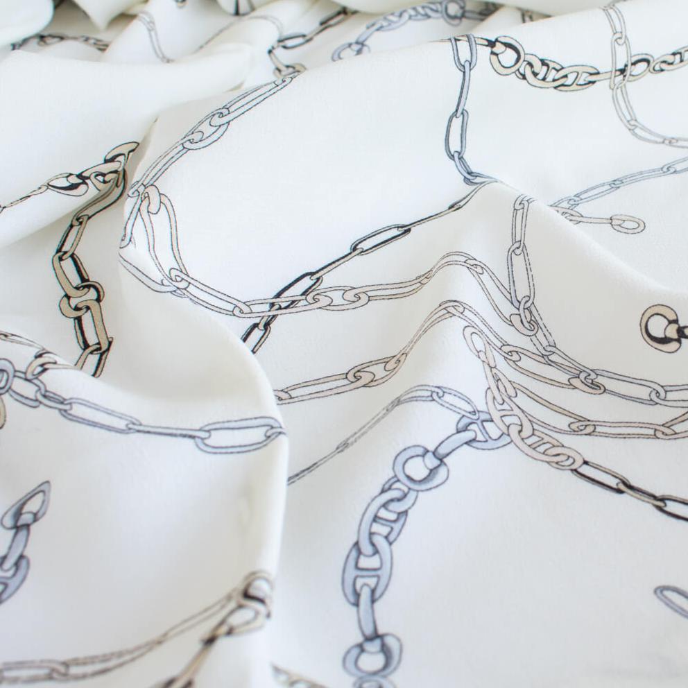 Famous Designer Chain Print Viscose Crepe Faille fabric by the yard. Chain links of tan and grey play upon an ivory background creating a whimsical yet sophisticated look. Slightly translucent with a lightly textured hand, this would make up gorgeous blouse or dress! Close up image.