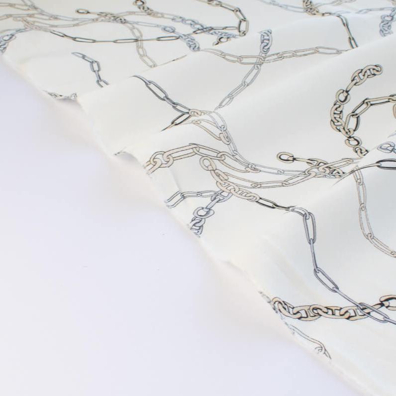 Famous Designer Chain Print Viscose Crepe Faille fabric by the yard. Chain links of tan and grey play upon an ivory background creating a whimsical yet sophisticated look. Slightly translucent with a lightly textured hand, this would make up gorgeous blouse or dress! Image of selvedge.