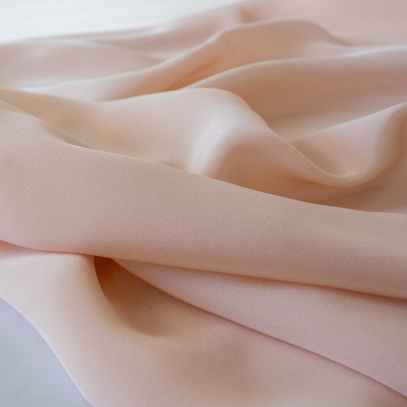 Universally flattering, this 100% Silk Crepe de Chine in a soft coral pink is such a versatile color. It's fluid drape is perfect for your next blouse or dress! Close up photo.