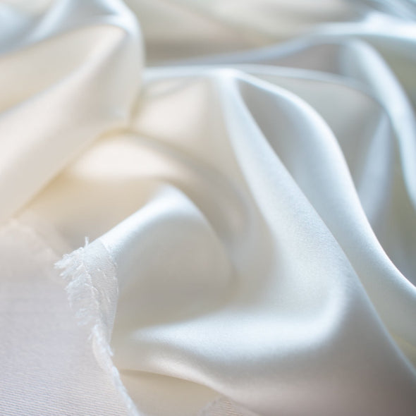 stretch silk charmeuse in a stunning alabaster shade of white.  Designer deadstock originally from a New York couture designer! You can enjoy the silkiness of a 93 % silk and 7% lycra in a easy to work with 53 inch width for one of your fancy frocks.  A popular fabric for creating fluid bias cut garments and luxurious lining to your special pieces like the French Jacket. Image of Selvedge edge.