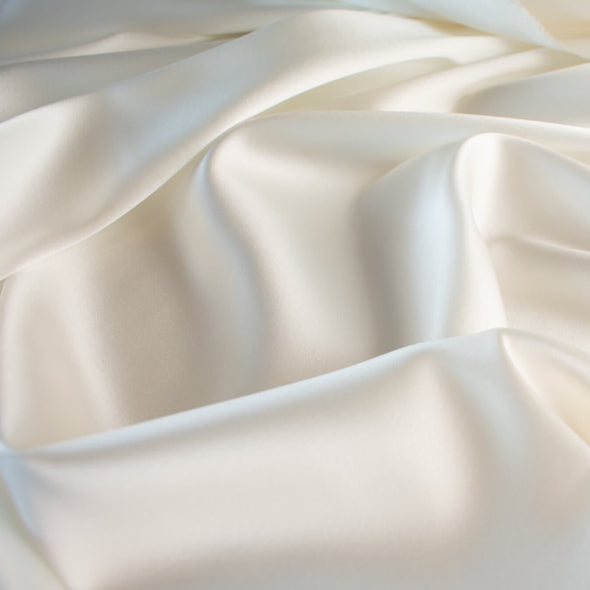 stretch silk charmeuse in a stunning alabaster shade of white.  Designer deadstock originally from a New York couture designer! You can enjoy the silkiness of a 93 % silk and 7% lycra in a easy to work with 53 inch width for one of your fancy frocks.  A popular fabric for creating fluid bias cut garments and luxurious lining to your special pieces like the French Jacket. Close up image.