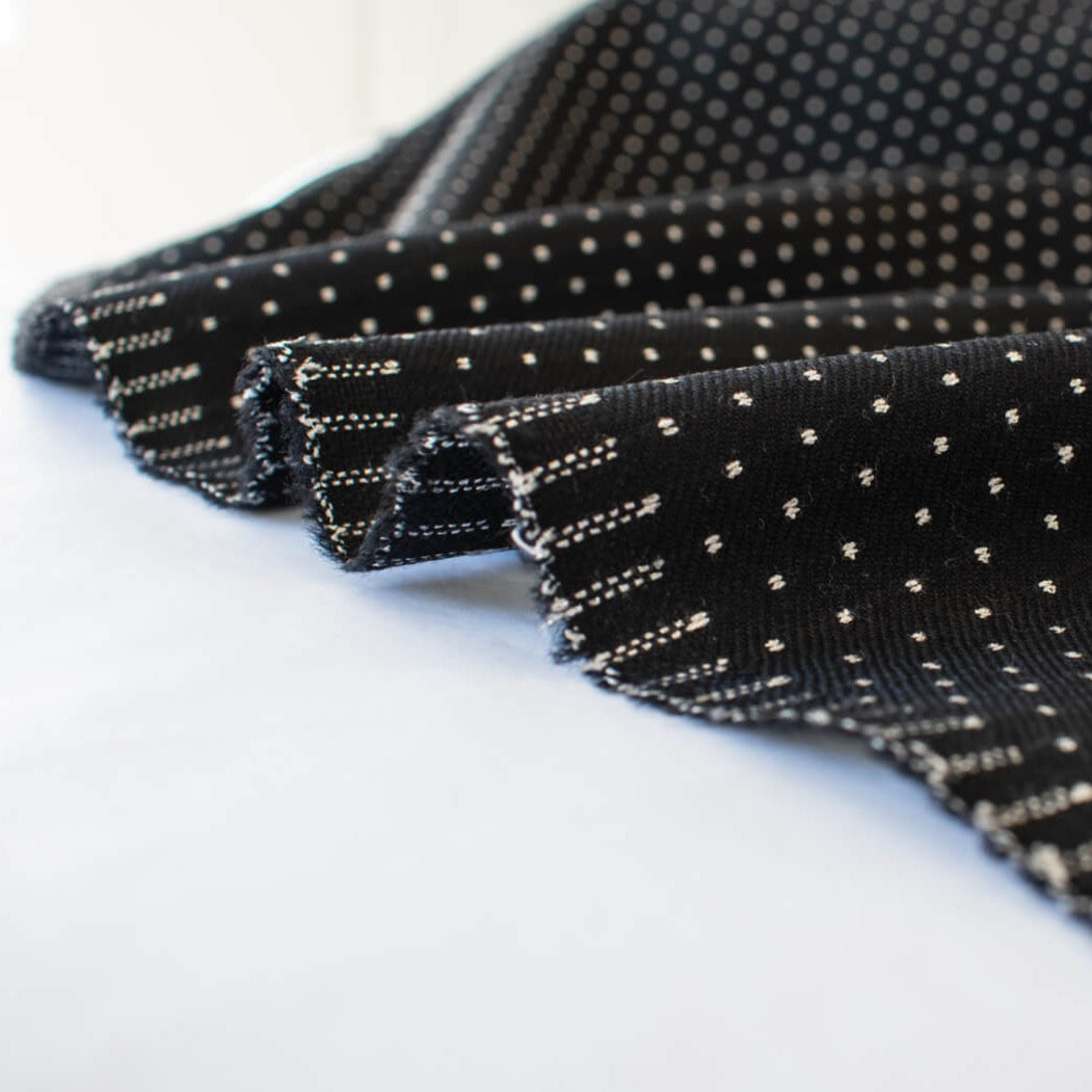 Luxurious designer suiting in black with a white and gold metallic running stitch. Take sophistication up a notch in this gorgeous wool blend with a soft and supple hand. Perfect for a glamorous tailored suit or jacket. Image of selvedge.