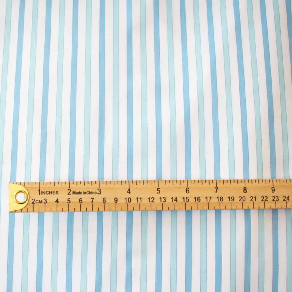 Designer striped cotton shirting that is soft, silky and "Fresh as Air"! White, powder blue and sky blue woven vertical stripes will bring a freshness to your style. Perfect for summer dresses, the classic shirtdress, a classic tailored shirt, or tunic. Image of fabric design scale with ruler.