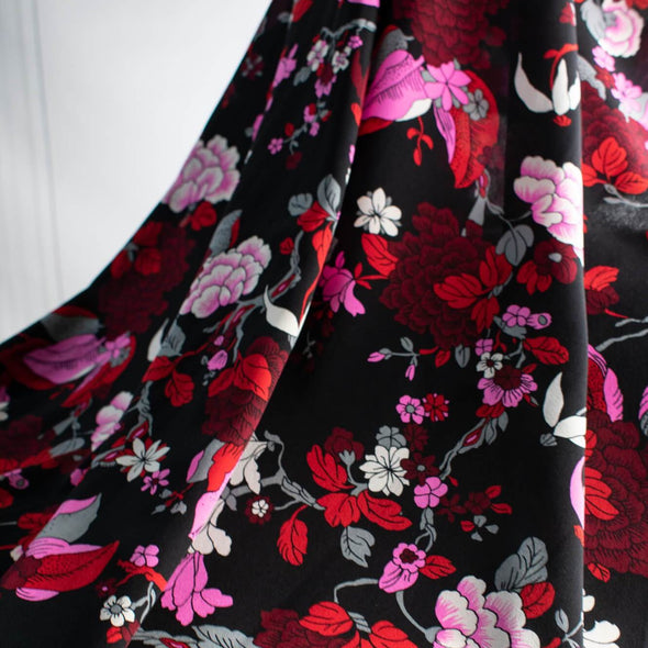 Create something stunning with this Designer Silk Crepe de Chine in florals of pinks, red, white, burgundy and grey upon a black background. Photo depicts fabric drape.