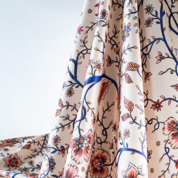 Silky rayon floral jacobean print . A vine in a gorgeous shade of electric blue trails through florals of various shades of peach, red and blue. Lengthwise drape photo.