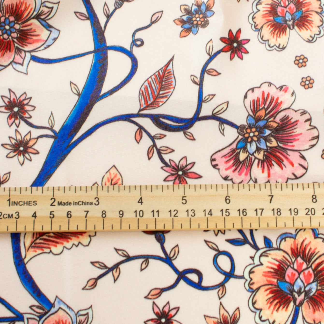 Silky rayon floral jacobean print . A vine in a gorgeous shade of electric blue trails through florals of various shades of peach, red and blue. Photo of fabric with ruler to show scale of floral design.