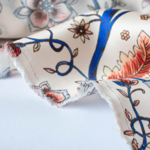 Silky rayon floral jacobean print . A vine in a gorgeous shade of electric blue trails through florals of various shades of peach, red and blue. Close up photo of selvedge.